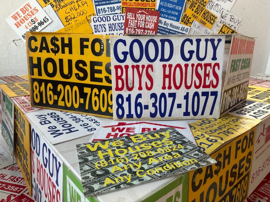 A collection of signs advertising cash for homes is shown earlier this month at an event in Kansas City, Missouri, celebrating a new state law regulating real estate wholesalers. Critics say these businesses can be predatory, especially for poor, minority and older homeowners. (Photo by Kevin Hardy/Stateline)
