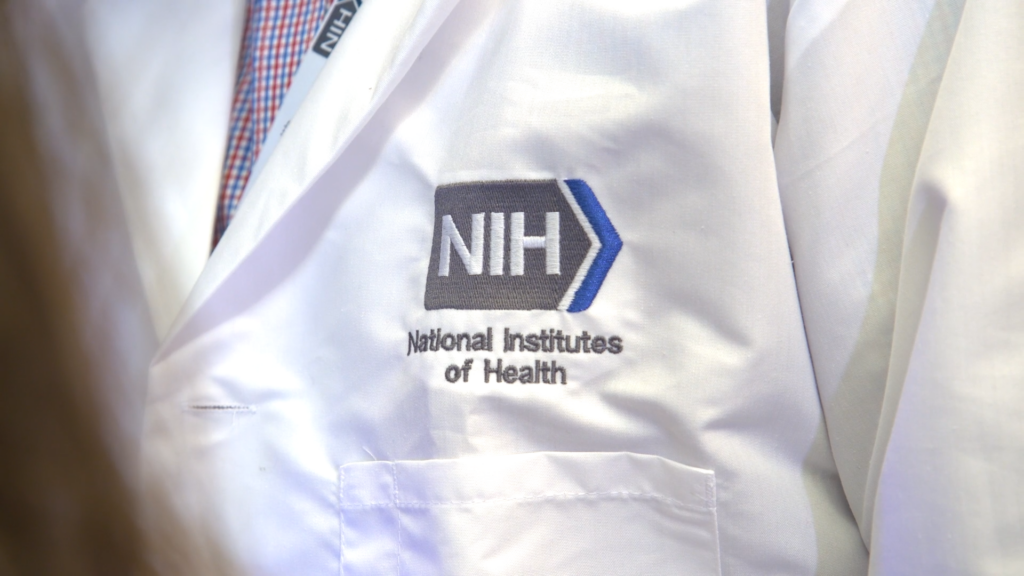 A National Institutes of Health researcher's lab jacket, embroidered with the NIH logo with blue chevron detail. (Photo courtesy NIH)